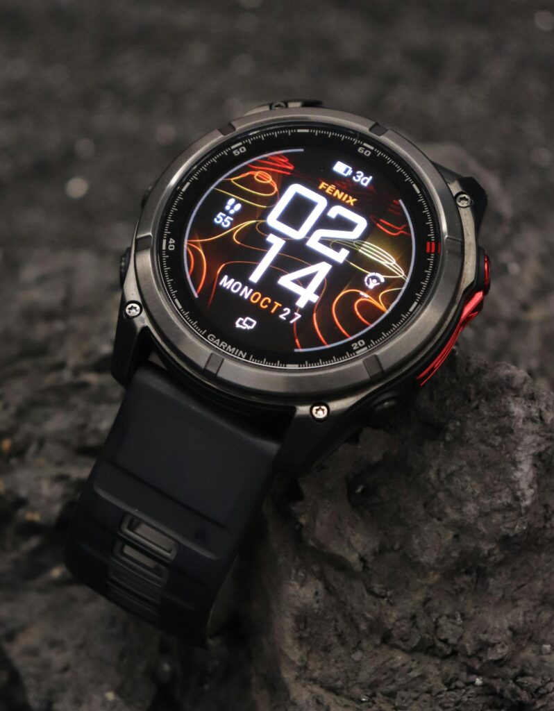 The Garmin Fenix 8 smartwatch with a rugged bezel and AMOLED display, positioned on a dark rock to highlight its outdoor durability.
