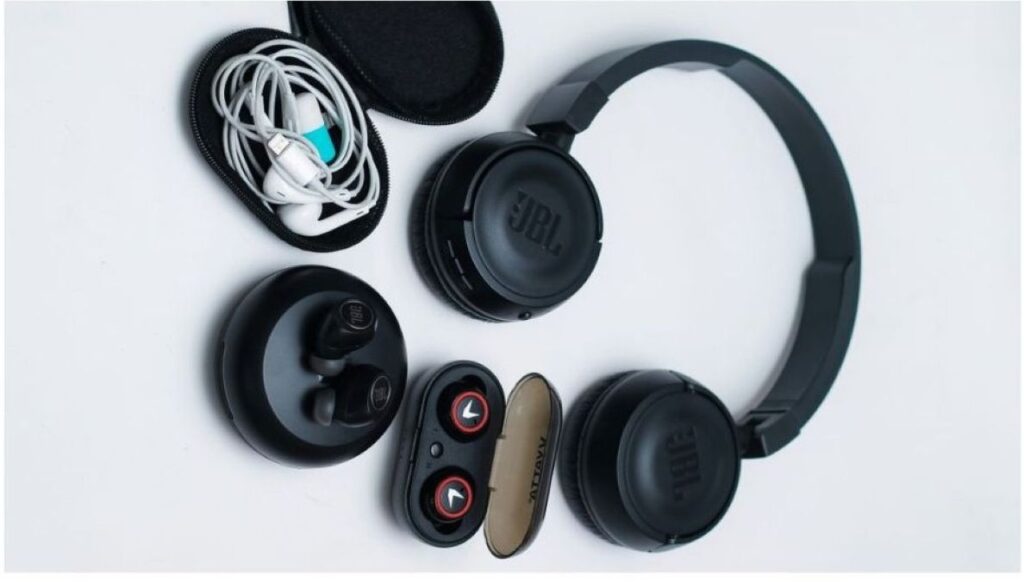 Two sets of wireless earbuds in open charging cases with over‑ear headphones and audio accessories arranged on a white surface.